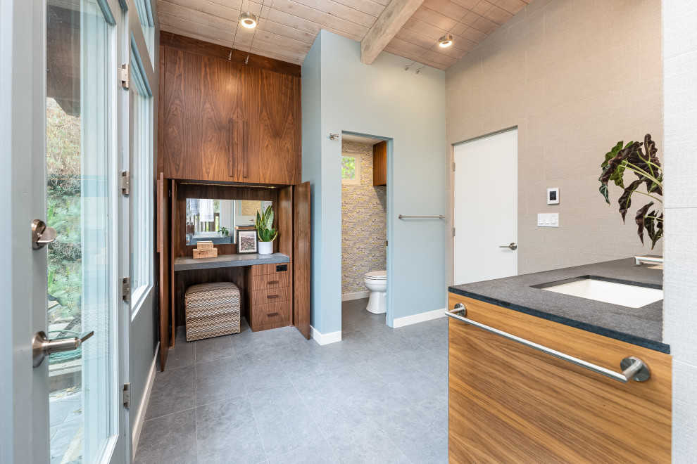 Cette image montre une salle de bain principale design de taille moyenne avec un placard à porte plane, une douche ouverte, un carrelage beige, des carreaux de porcelaine, un mur bleu, un sol en carrelage de porcelaine, un lavabo encastré, un plan de toilette en quartz modifié, un sol gris, une cabine de douche à porte battante, un plan de toilette gris, un banc de douche, meuble double vasque, meuble-lavabo suspendu et poutres apparentes.