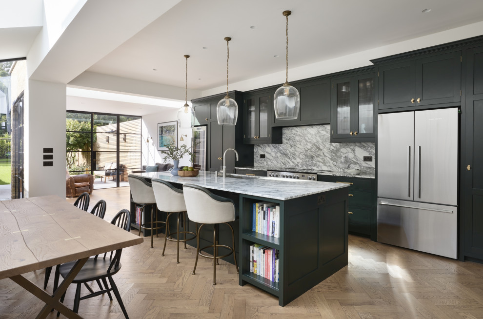 Large traditional galley kitchen/diner in London with a submerged sink, shaker cabinets, green cabinets, marble worktops, grey splashback, marble splashback, stainless steel appliances, an island, grey worktops, light hardwood flooring and beige floors.