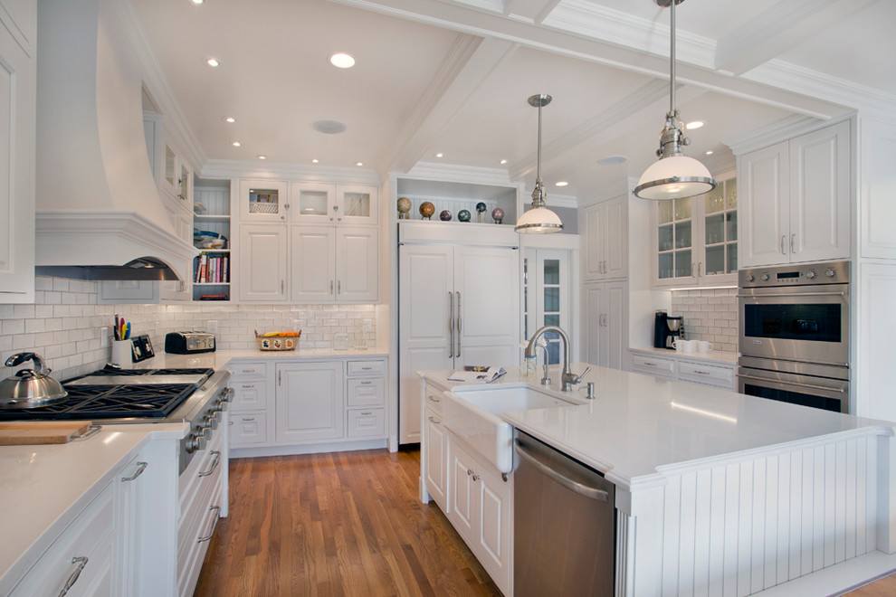 Large transitional l-shaped medium tone wood floor eat-in kitchen photo with a farmhouse sink, white cabinets, granite countertops, white backsplash, stainless steel appliances, an island, raised-panel cabinets and subway tile backsplash