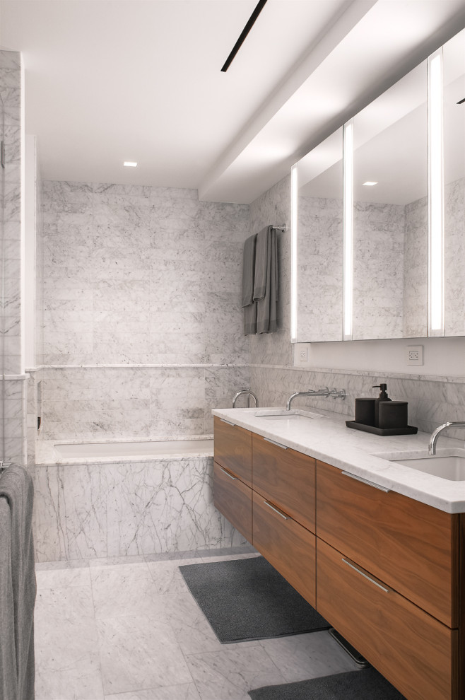 Inspiration for a medium sized modern ensuite bathroom in New York with freestanding cabinets, medium wood cabinets, a submerged bath, an alcove shower, grey tiles, marble tiles, marble flooring, a submerged sink, marble worktops, grey floors, a hinged door, white worktops, a shower bench, double sinks and a floating vanity unit.