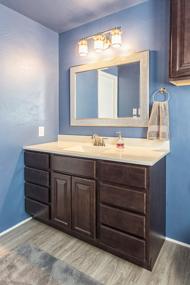 Photo of a small transitional kids bathroom in Austin with raised-panel cabinets, dark wood cabinets, blue walls, laminate floors, an integrated sink and solid surface benchtops.