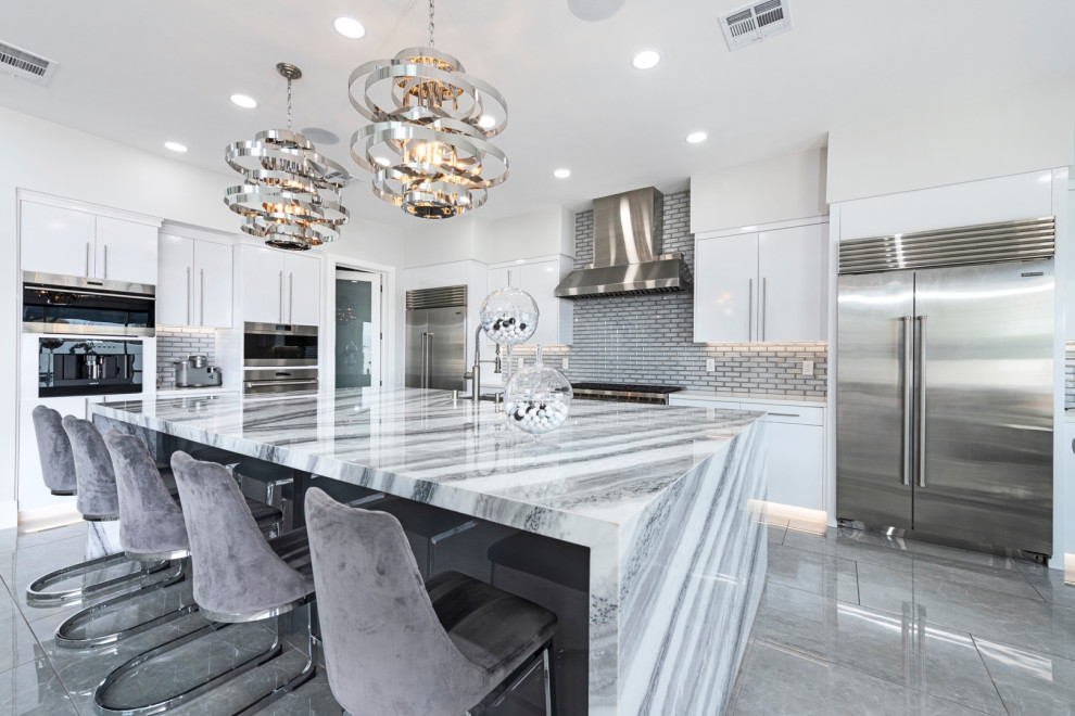 Inspiration for an expansive contemporary galley open plan kitchen in Las Vegas with an undermount sink, flat-panel cabinets, white cabinets, granite benchtops, glass tile splashback, stainless steel appliances, ceramic floors, with island, grey floor and white benchtop.