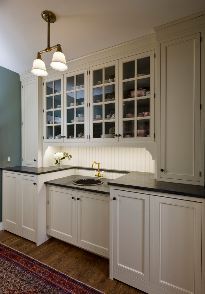Design ideas for a small traditional single-wall utility room in Chicago with a single-bowl sink, beaded inset cabinets, white cabinets, soapstone benchtops, green walls, medium hardwood floors, a concealed washer and dryer and black benchtop.