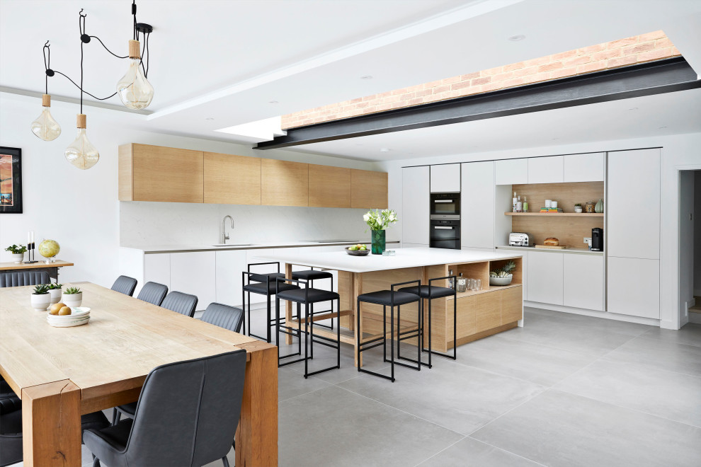 Photo of an expansive scandinavian l-shaped open plan kitchen in Surrey with white cabinets, quartzite benchtops, white splashback, marble splashback, black appliances, ceramic floors, with island, grey floor, white benchtop and flat-panel cabinets.