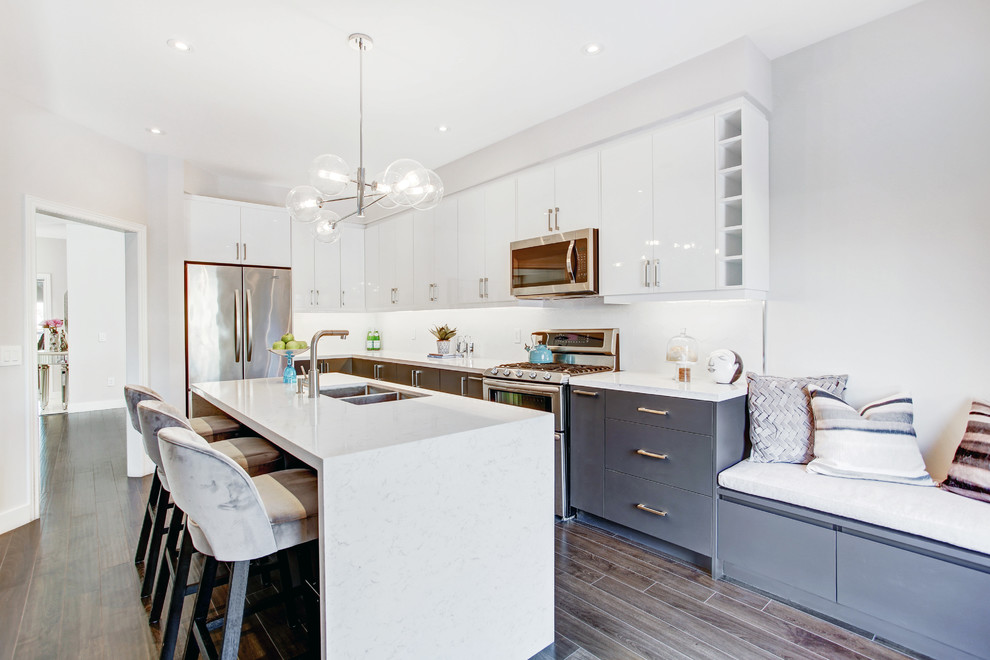 Example of a mid-sized transitional l-shaped dark wood floor and brown floor kitchen design in Toronto with an undermount sink, flat-panel cabinets, gray cabinets, white backsplash, stainless steel appliances and an island