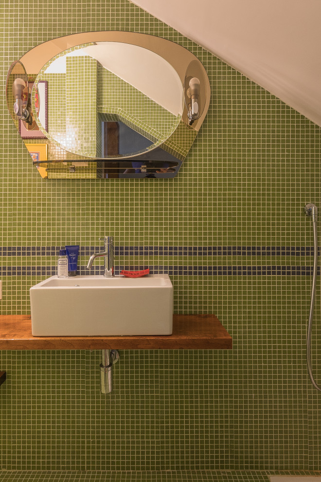 Modelo de aseo contemporáneo pequeño con sanitario de una pieza, baldosas y/o azulejos verdes, baldosas y/o azulejos en mosaico, paredes blancas, suelo con mosaicos de baldosas, lavabo sobreencimera, encimera de madera y suelo verde