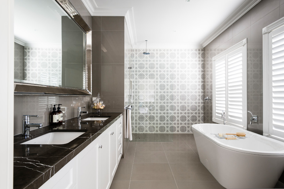 This is an example of a transitional master bathroom in Melbourne with recessed-panel cabinets, white cabinets, a freestanding tub, a curbless shower, beige tile, white tile, brown walls, an undermount sink, brown floor, an open shower and black benchtops.