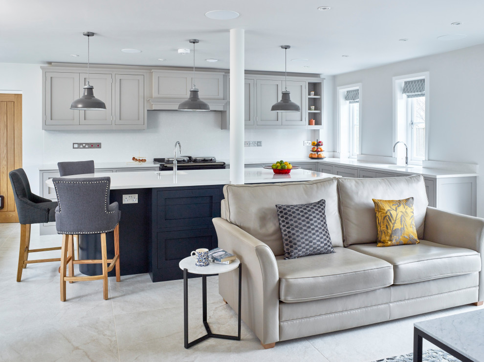 Large contemporary open plan kitchen in Oxfordshire with an integrated sink, shaker cabinets, blue cabinets, quartzite benchtops, white splashback, stone slab splashback, black appliances, porcelain floors, with island, white floor and white benchtop.