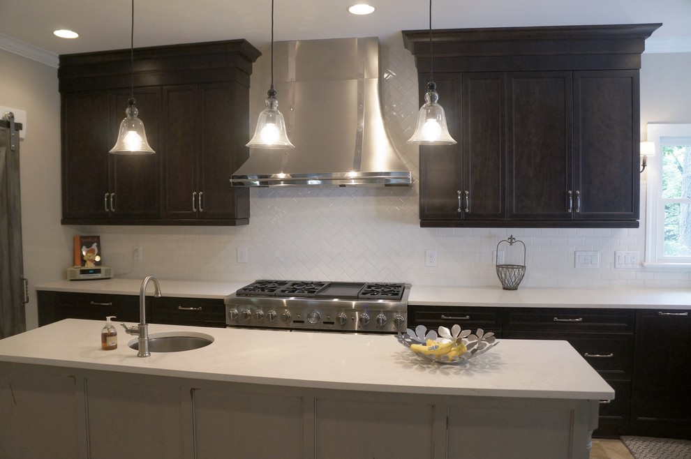 Mid-sized transitional l-shaped travertine floor eat-in kitchen photo in Raleigh with a farmhouse sink, flat-panel cabinets, dark wood cabinets, quartz countertops, white backsplash, ceramic backsplash, stainless steel appliances and an island