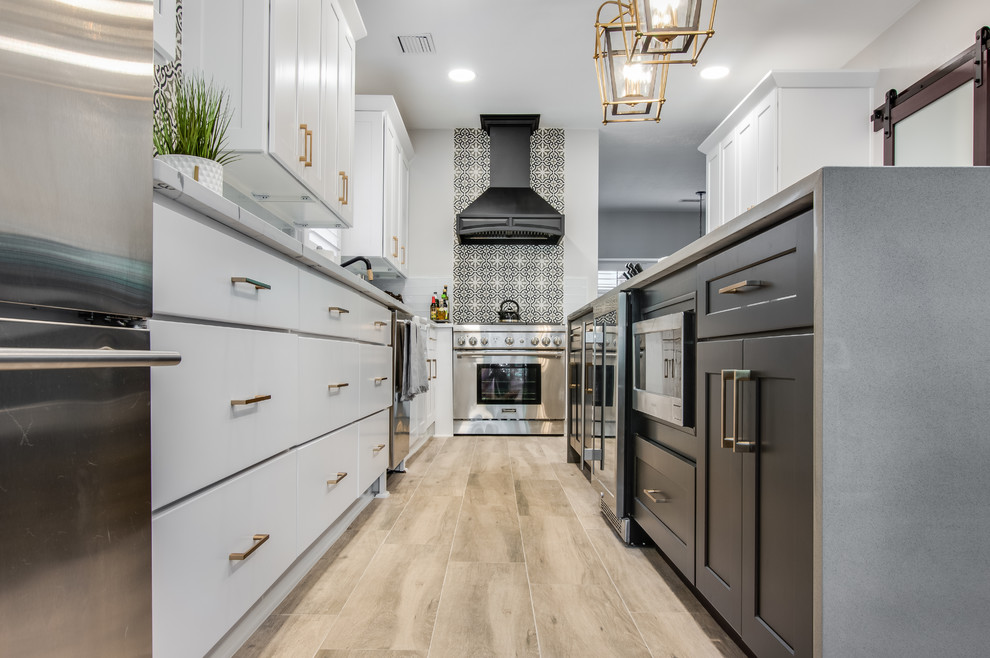 Inspiration for a large transitional l-shaped porcelain tile and gray floor kitchen pantry remodel in Houston with a farmhouse sink, shaker cabinets, white cabinets, quartzite countertops, white backsplash, glass tile backsplash, stainless steel appliances, an island and white countertops
