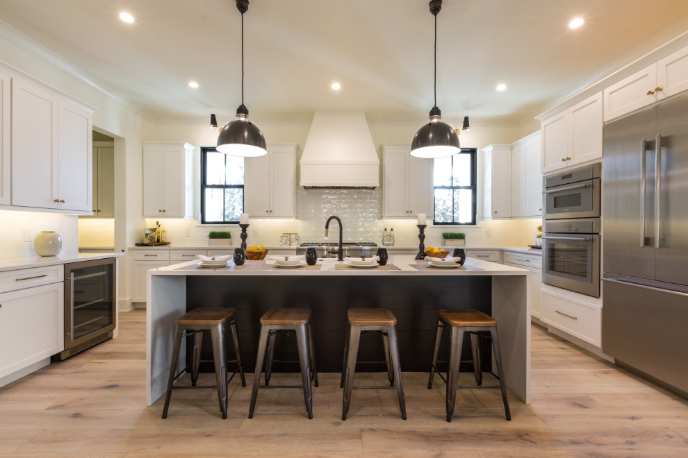 Inspiration for a mid-sized country u-shaped eat-in kitchen in Orlando with a farmhouse sink, shaker cabinets, white cabinets, quartz benchtops, white splashback, ceramic splashback, stainless steel appliances, medium hardwood floors, with island, brown floor and white benchtop.