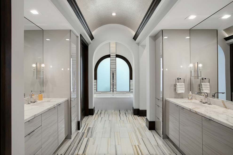 This is an example of a contemporary master bathroom in Houston with flat-panel cabinets, grey cabinets, a drop-in tub, white walls, an undermount sink, marble benchtops, multi-coloured floor, an enclosed toilet, a double vanity and a built-in vanity.