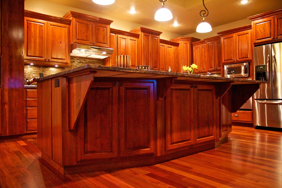 Inspiration for a large l-shaped medium tone wood floor open concept kitchen remodel with an undermount sink, raised-panel cabinets, dark wood cabinets, multicolored backsplash, glass tile backsplash, stainless steel appliances and an island