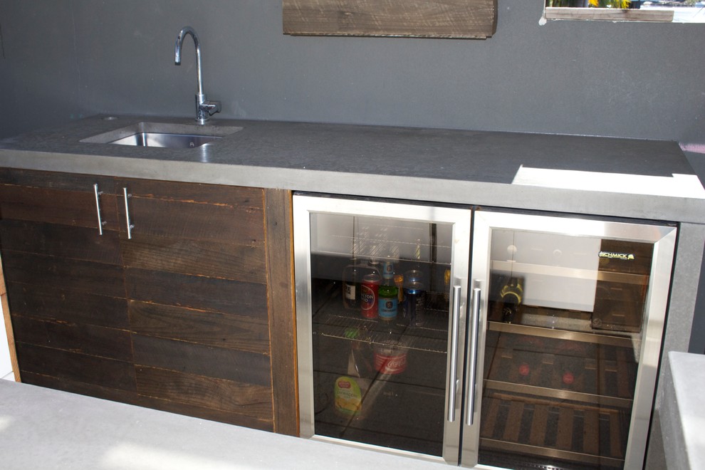 This is an example of a small beach style galley seated home bar in Gold Coast - Tweed with an undermount sink, flat-panel cabinets, dark wood cabinets, concrete benchtops and grey splashback.