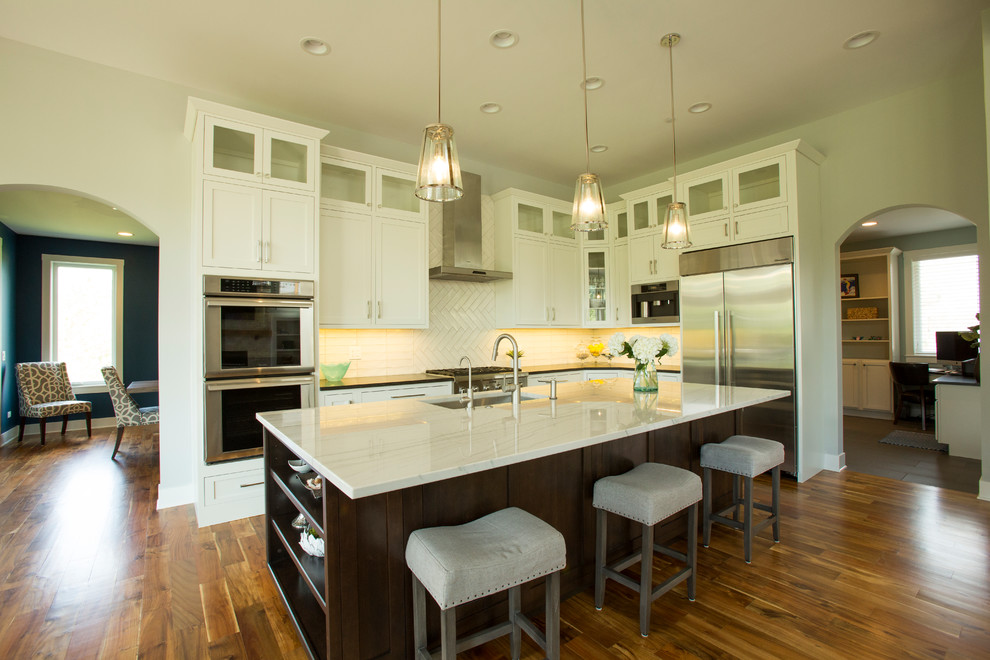 Design ideas for a large eclectic eat-in kitchen in Chicago with an undermount sink, flat-panel cabinets, white cabinets, granite benchtops, white splashback, ceramic splashback, stainless steel appliances, medium hardwood floors and with island.