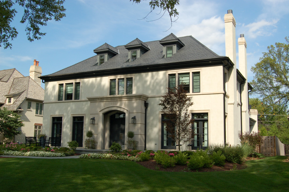 This is an example of a large traditional two-storey stucco house exterior in Chicago with a hip roof, a shingle roof and a grey roof.