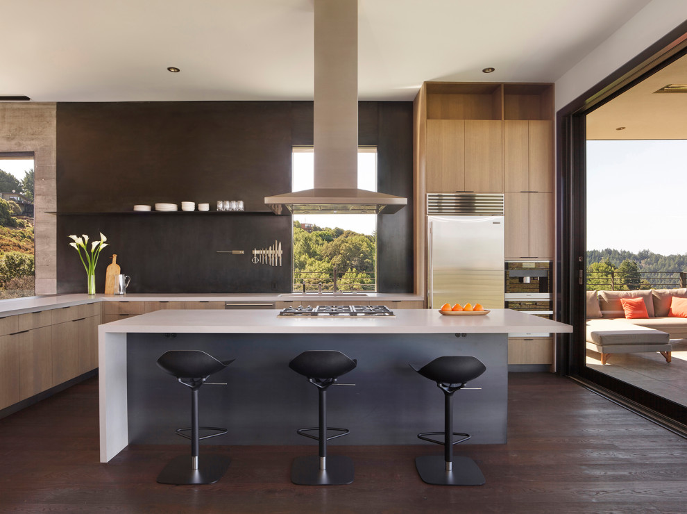 Medium sized modern l-shaped open plan kitchen in San Francisco with flat-panel cabinets, medium wood cabinets, engineered stone countertops, stainless steel appliances, dark hardwood flooring, an island, grey floors, white worktops, a submerged sink, black splashback and a feature wall.