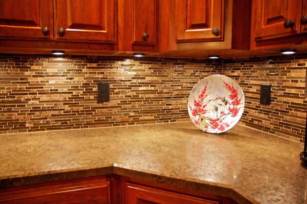 Example of a large l-shaped medium tone wood floor open concept kitchen design with an undermount sink, raised-panel cabinets, dark wood cabinets, multicolored backsplash, glass tile backsplash, stainless steel appliances and an island