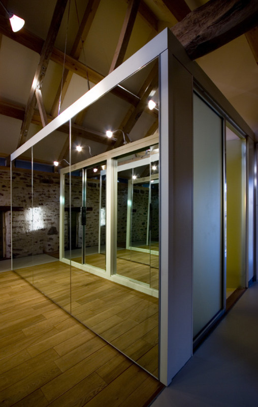 Photo of a small contemporary gender neutral wardrobe in West Midlands with glass-front cabinets and light hardwood flooring.