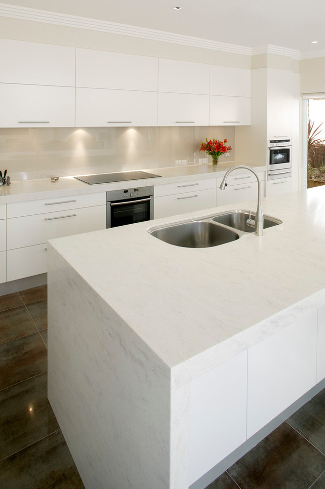 This is an example of a contemporary l-shaped eat-in kitchen in Sydney with an undermount sink, flat-panel cabinets, white cabinets and glass sheet splashback.