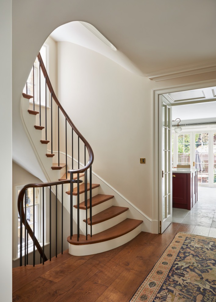 Пример оригинального дизайна: большая изогнутая лестница в классическом стиле с деревянными ступенями, крашенными деревянными подступенками и перилами из смешанных материалов