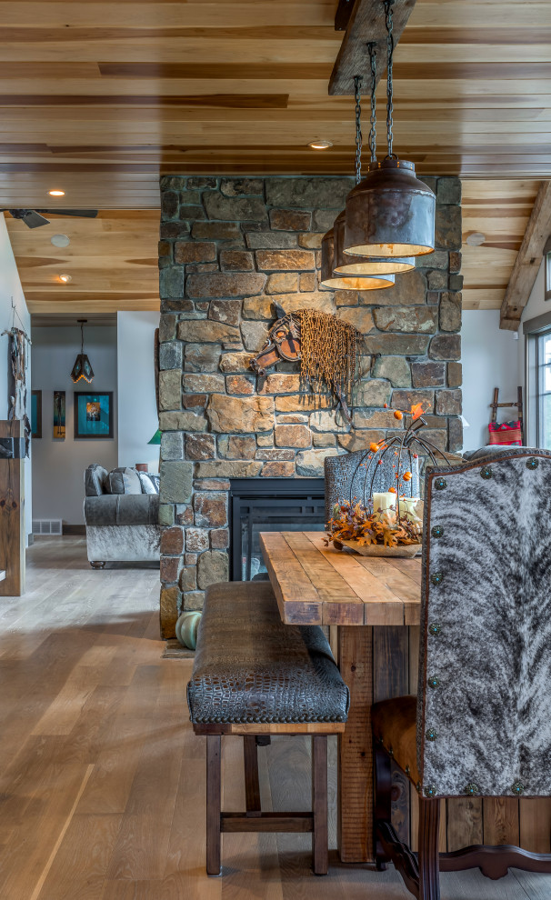 Idée de décoration pour une grande salle à manger ouverte sur la cuisine sud-ouest américain avec un mur gris, parquet clair, une cheminée double-face, un manteau de cheminée en pierre, un sol marron et un plafond en bois.