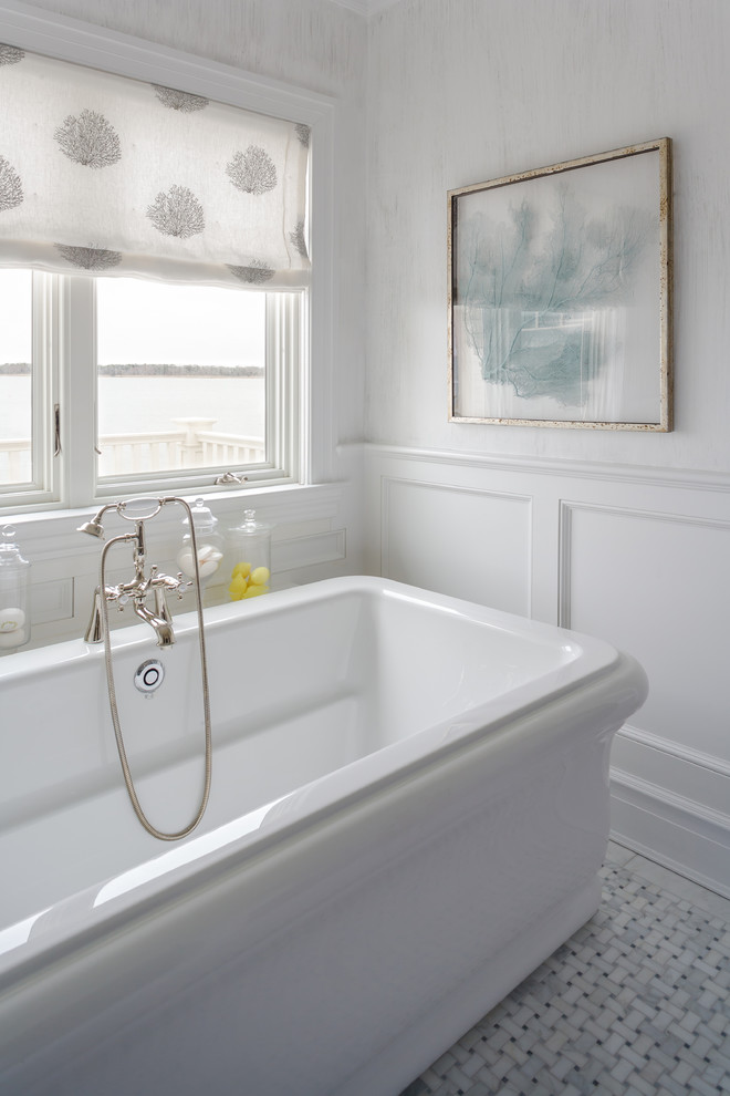 This is an example of a mid-sized transitional bathroom in New York with a freestanding tub, recessed-panel cabinets, grey cabinets, white walls, marble floors and an undermount sink.