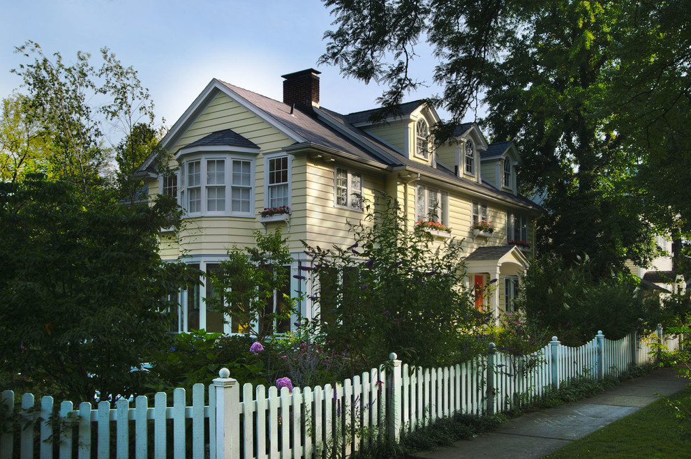 This is an example of a large traditional two-storey yellow exterior in Cleveland with vinyl siding and a clipped gable roof.