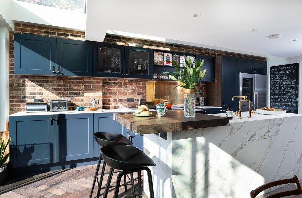 Design ideas for a mid-sized modern galley eat-in kitchen in Other with an integrated sink, shaker cabinets, blue cabinets, quartz benchtops, metallic splashback, metal splashback, black appliances, painted wood floors, with island, brown floor and white benchtop.