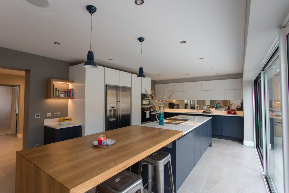 Design ideas for an expansive contemporary l-shaped eat-in kitchen in Hertfordshire with a drop-in sink, flat-panel cabinets, blue cabinets, quartzite benchtops, metallic splashback, mirror splashback, stainless steel appliances, porcelain floors, with island, white floor and white benchtop.