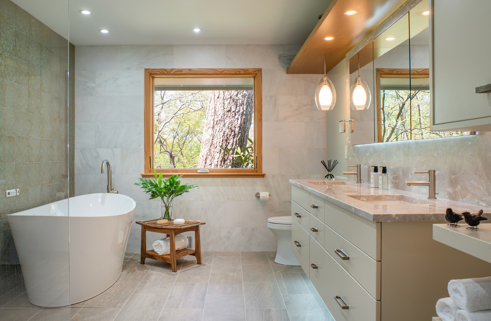 Photo of a large contemporary master bathroom in DC Metro with flat-panel cabinets, beige cabinets, a freestanding tub, beige tile, marble, beige walls, linoleum floors, an undermount sink, marble benchtops, beige floor, beige benchtops and a one-piece toilet.