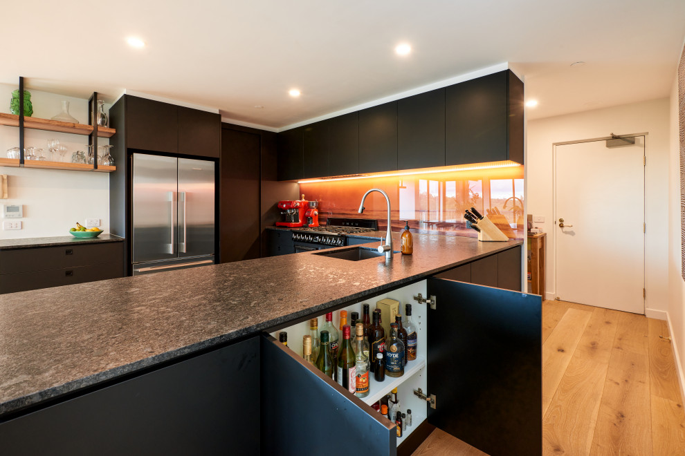 Immagine di una cucina moderna di medie dimensioni con ante lisce, ante nere, top in quarzo composito, paraspruzzi arancione, paraspruzzi con lastra di vetro, elettrodomestici neri e top nero