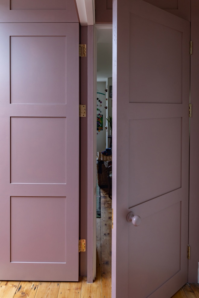 На фото: открытая гостиная комната среднего размера в стиле фьюжн с с книжными шкафами и полками, розовыми стенами, паркетным полом среднего тона, скрытым телевизором и панелями на части стены