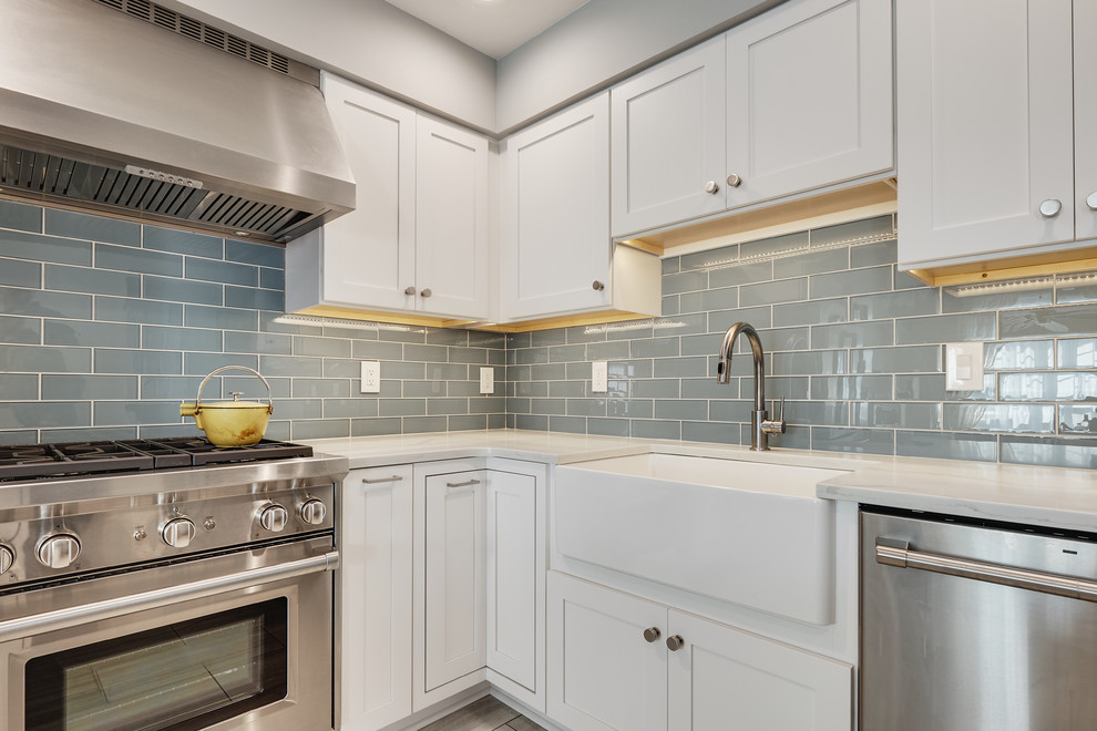 Small modern l-shaped separate kitchen in Philadelphia with a farmhouse sink, recessed-panel cabinets, white cabinets, quartz benchtops, blue splashback, glass tile splashback, stainless steel appliances, vinyl floors, with island, beige floor and white benchtop.