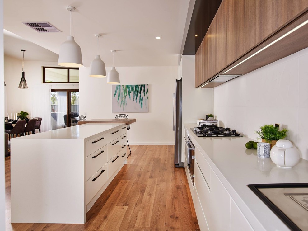 This is an example of a large scandinavian galley kitchen pantry in Other with a drop-in sink, flat-panel cabinets, white cabinets, quartz benchtops, white splashback, ceramic splashback, stainless steel appliances, medium hardwood floors, with island, brown floor and white benchtop.