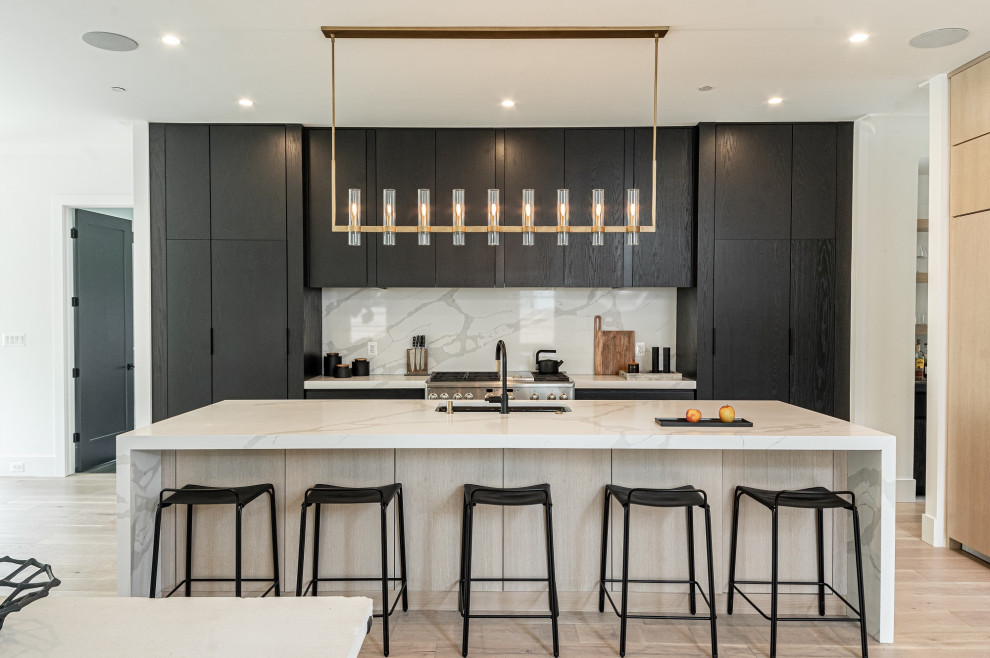 Inspiration for a medium sized contemporary galley kitchen in DC Metro with flat-panel cabinets, black cabinets, engineered stone countertops, an island, white worktops, a submerged sink, white splashback, metro tiled splashback, stainless steel appliances, light hardwood flooring and beige floors.