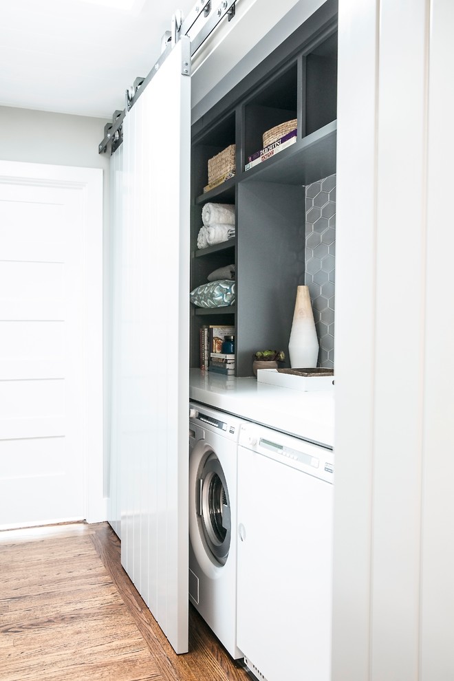 Inspiration for a small contemporary single-wall laundry cupboard in San Francisco with open cabinets, grey cabinets, solid surface benchtops, grey walls, medium hardwood floors and a side-by-side washer and dryer.