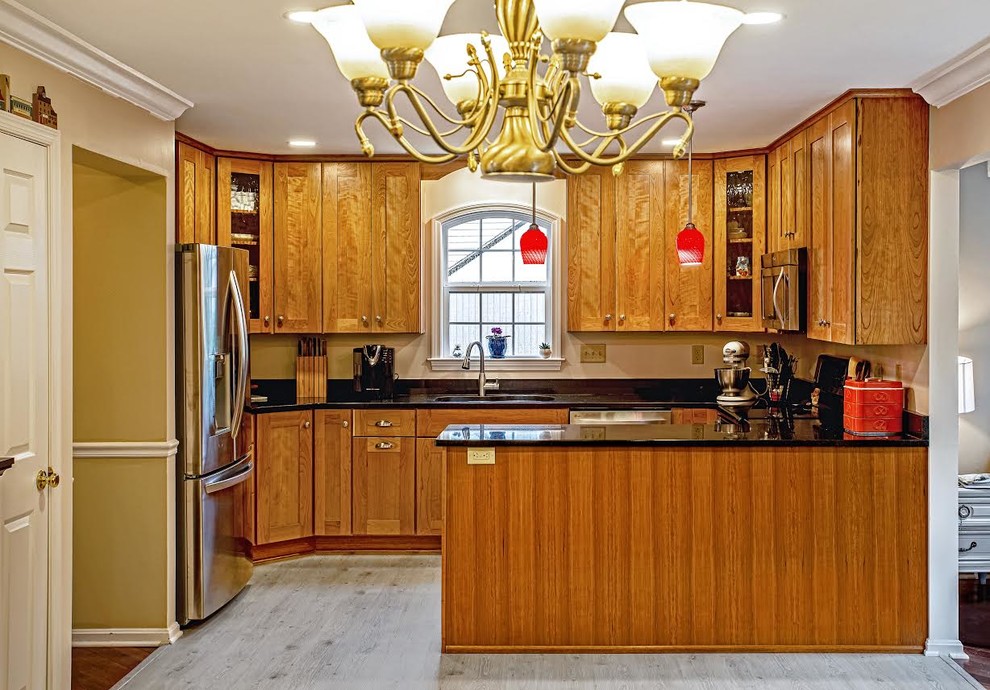 Inspiration for a traditional u-shaped eat-in kitchen in Baltimore with a double-bowl sink, shaker cabinets, medium wood cabinets, granite benchtops, stainless steel appliances, vinyl floors, a peninsula, grey floor and black benchtop.