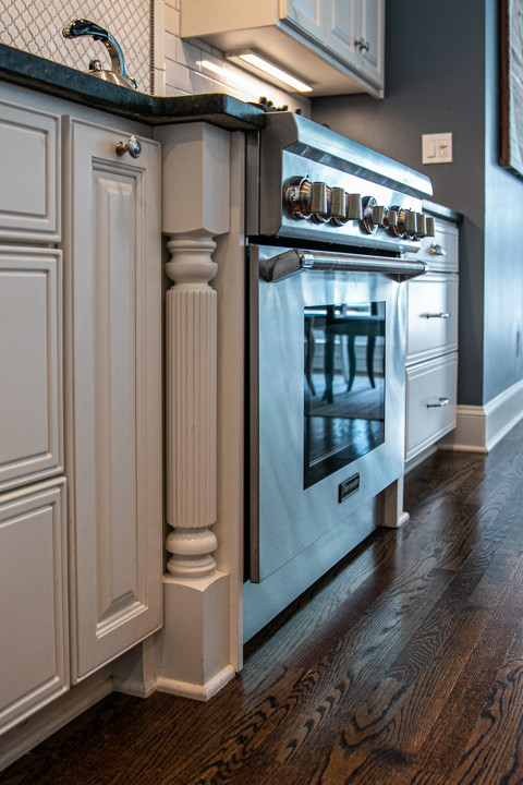 Large transitional l-shaped medium tone wood floor and brown floor open concept kitchen photo in Charlotte with a farmhouse sink, white cabinets, granite countertops, white backsplash, stainless steel appliances, an island, raised-panel cabinets, porcelain backsplash and white countertops