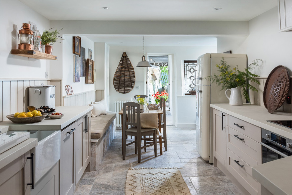 Photo of a mid-sized beach style u-shaped eat-in kitchen in Devon with a farmhouse sink, recessed-panel cabinets, beige cabinets, beige splashback, stainless steel appliances, grey floor and beige benchtop.