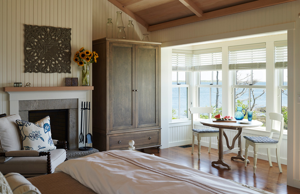 This is an example of a beach style master bedroom in Portland Maine with white walls and medium hardwood floors.
