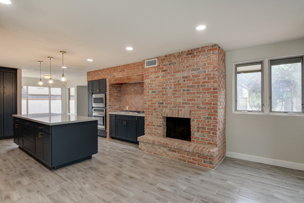 Mid-sized transitional u-shaped porcelain tile and gray floor eat-in kitchen photo in Phoenix with a farmhouse sink, shaker cabinets, blue cabinets, quartz countertops, red backsplash, brick backsplash, stainless steel appliances, an island and white countertops