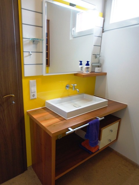 This is an example of a traditional powder room in Stuttgart with flat-panel cabinets, white cabinets, a wall-mount toilet, yellow tile, glass sheet wall, yellow walls, cork floors and wood benchtops.