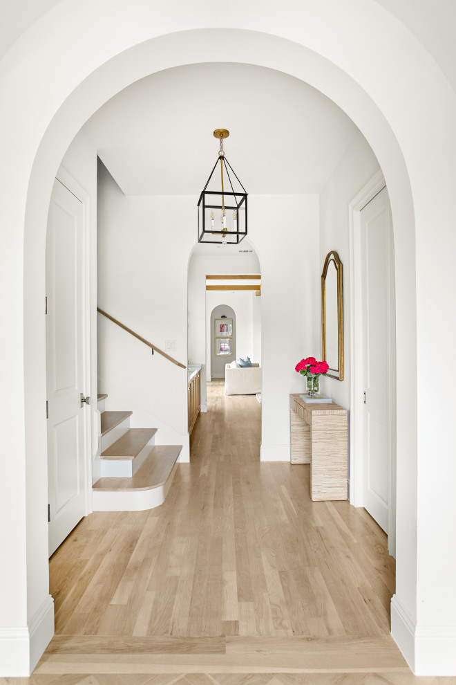 Cette photo montre un grand hall d'entrée chic avec un mur blanc, parquet clair, une porte simple, une porte métallisée et un sol marron.