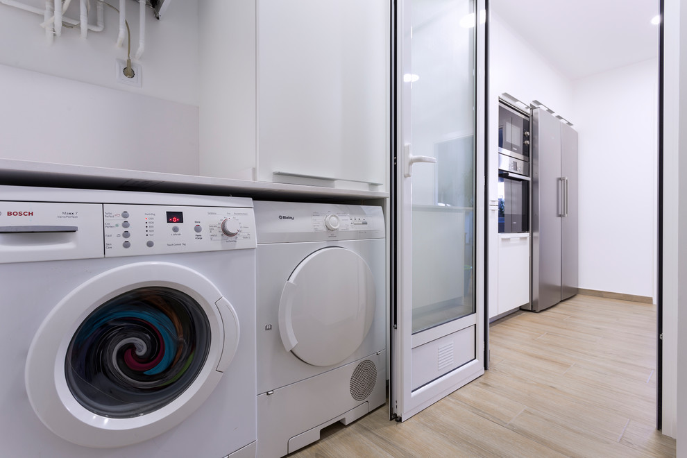 Photo of a mid-sized transitional laundry room in Barcelona with a single-bowl sink, flat-panel cabinets, light wood cabinets and white splashback.