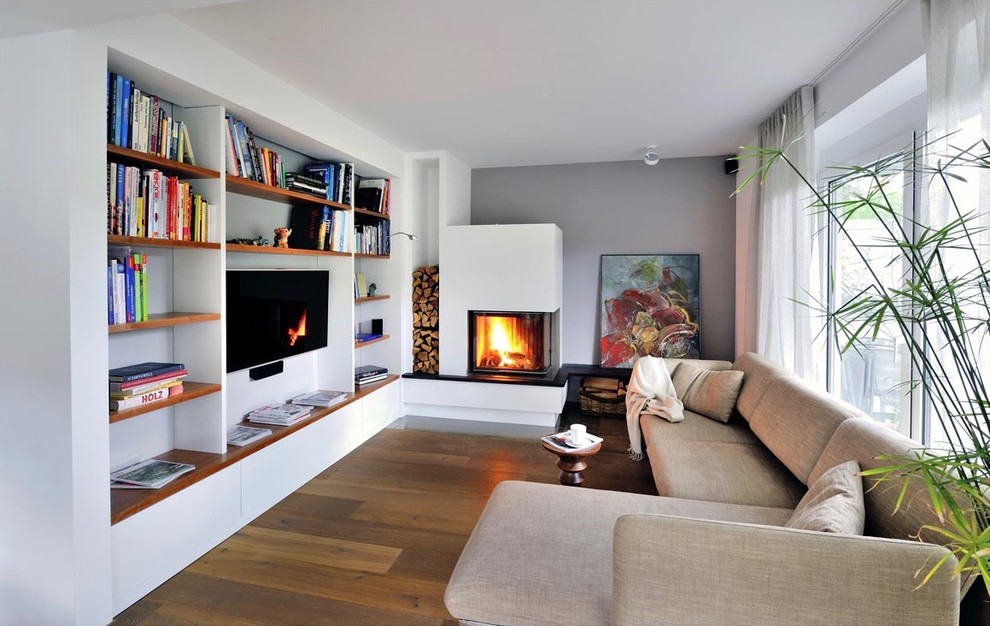 Design ideas for an expansive contemporary open concept family room in Munich with white walls, a standard fireplace, a plaster fireplace surround, a wall-mounted tv, a library, dark hardwood floors and brown floor.