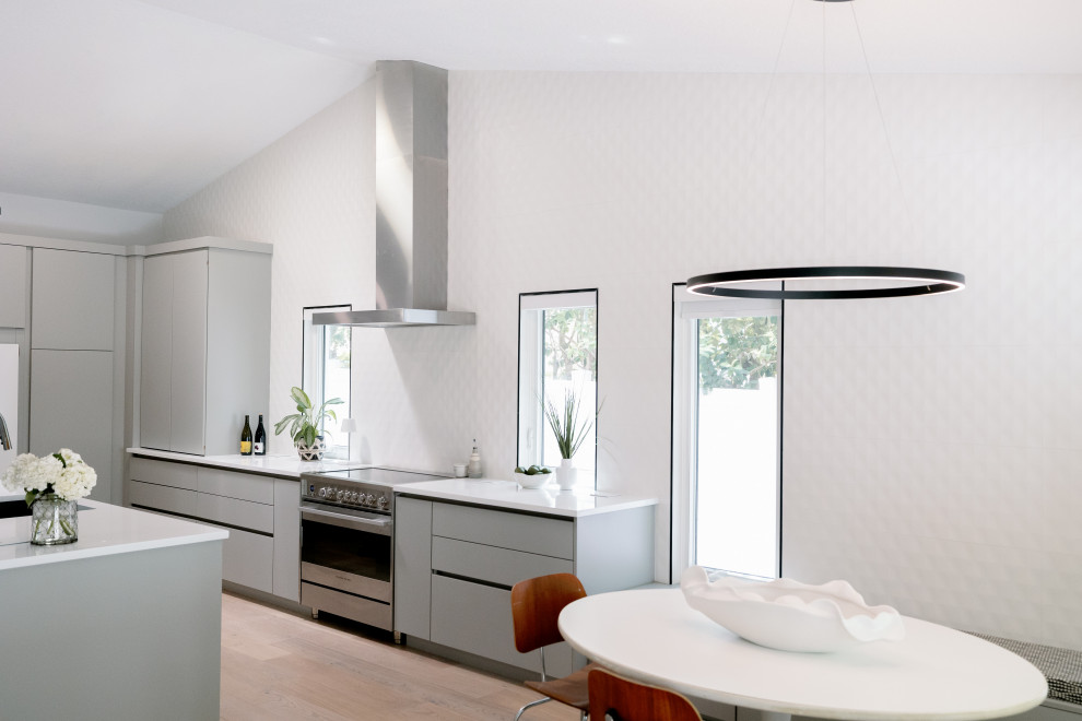 Design ideas for a mid-sized midcentury galley eat-in kitchen in Orlando with a drop-in sink, flat-panel cabinets, grey cabinets, quartz benchtops, white splashback, ceramic splashback, stainless steel appliances, light hardwood floors, with island, brown floor, white benchtop and vaulted.