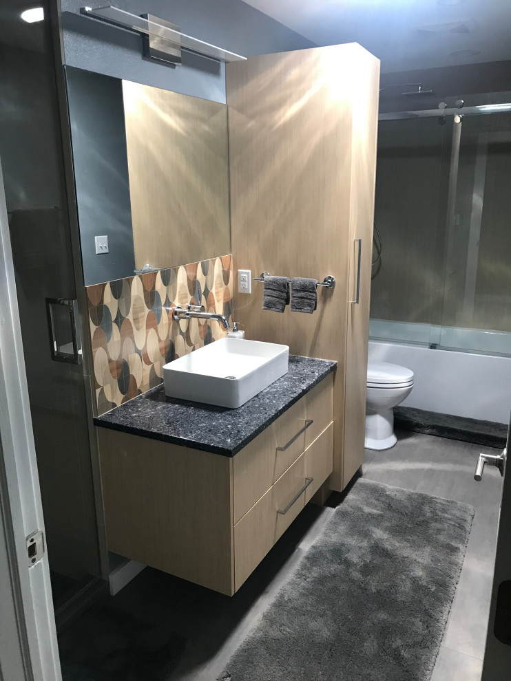 Photo of a mid-sized modern kids bathroom in Milwaukee with flat-panel cabinets, light wood cabinets, an alcove tub, an alcove shower, a one-piece toilet, beige tile, porcelain tile, blue walls, porcelain floors, a vessel sink, quartzite benchtops, grey floor, a hinged shower door and blue benchtops.