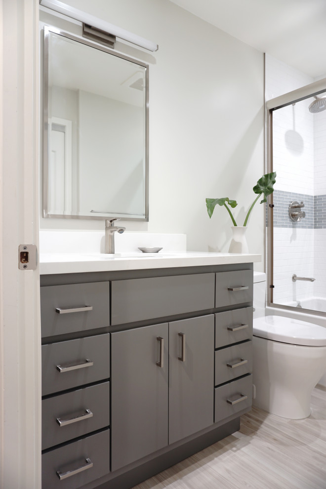 This is an example of a mid-sized contemporary bathroom in San Francisco with flat-panel cabinets, grey cabinets, an alcove tub, a shower/bathtub combo, a one-piece toilet, white tile, subway tile, white walls, wood-look tile, an undermount sink, engineered quartz benchtops, beige floor, a sliding shower screen, white benchtops, a niche, a single vanity and a built-in vanity.