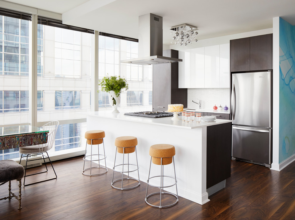 This is an example of a contemporary galley open plan kitchen in Chicago with flat-panel cabinets, dark wood cabinets, white splashback, mosaic tile splashback, stainless steel appliances, dark hardwood floors, a peninsula and brown floor.